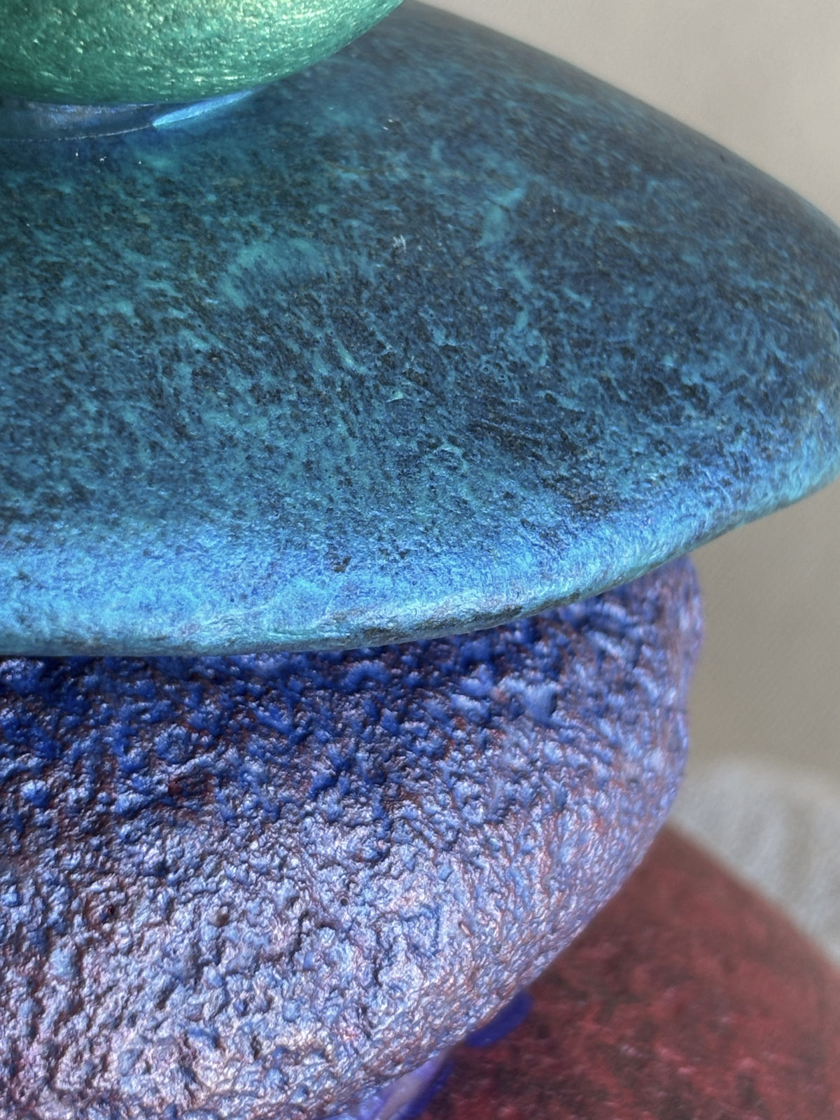 Blue metallic jewel tones visible on a smooth river rock sculpture by Robert Schott