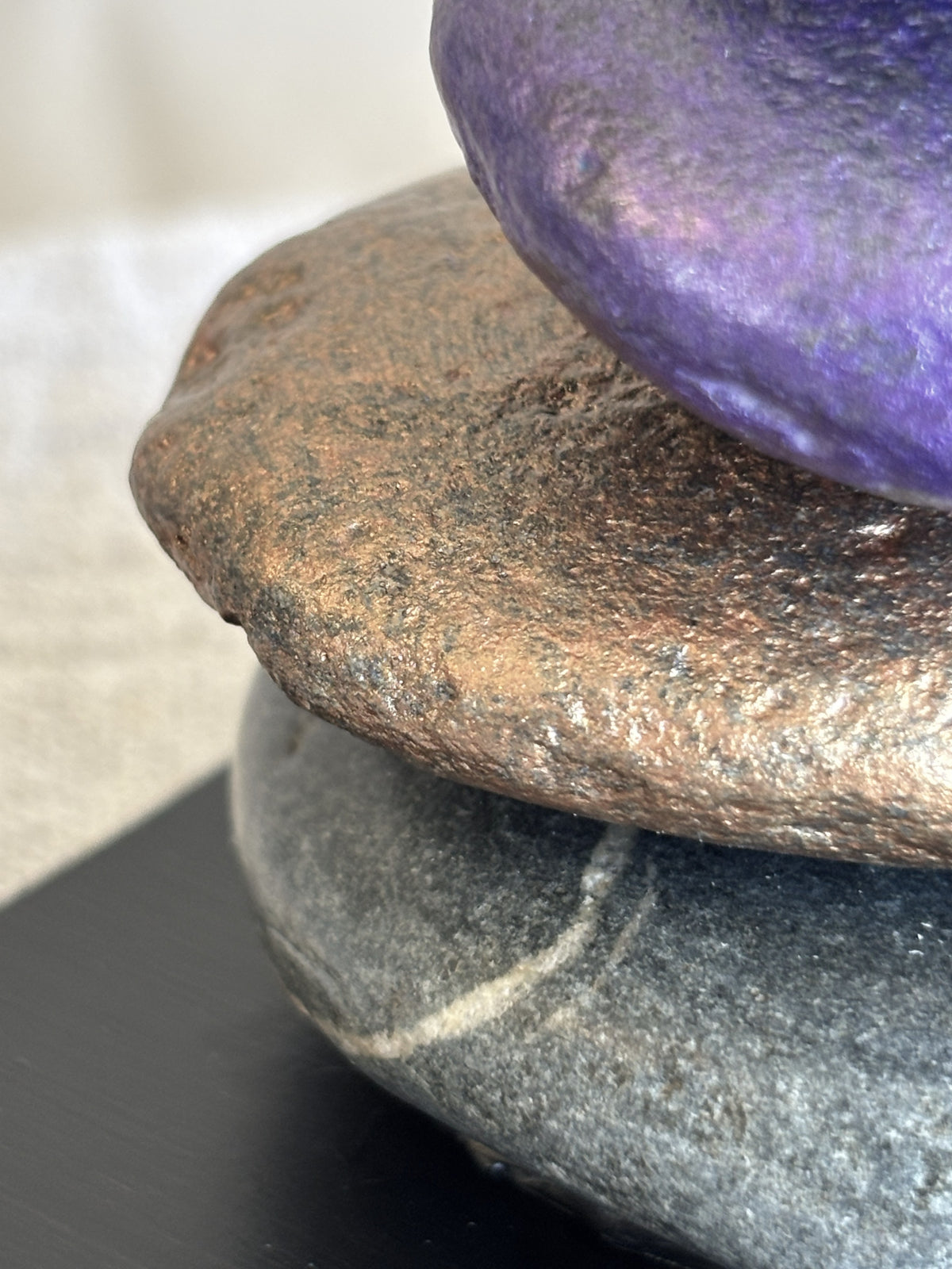 Charcoal, bronze and purple metallic jewel tone colored very closeup from a stacked stone sculpture by Robert Schott