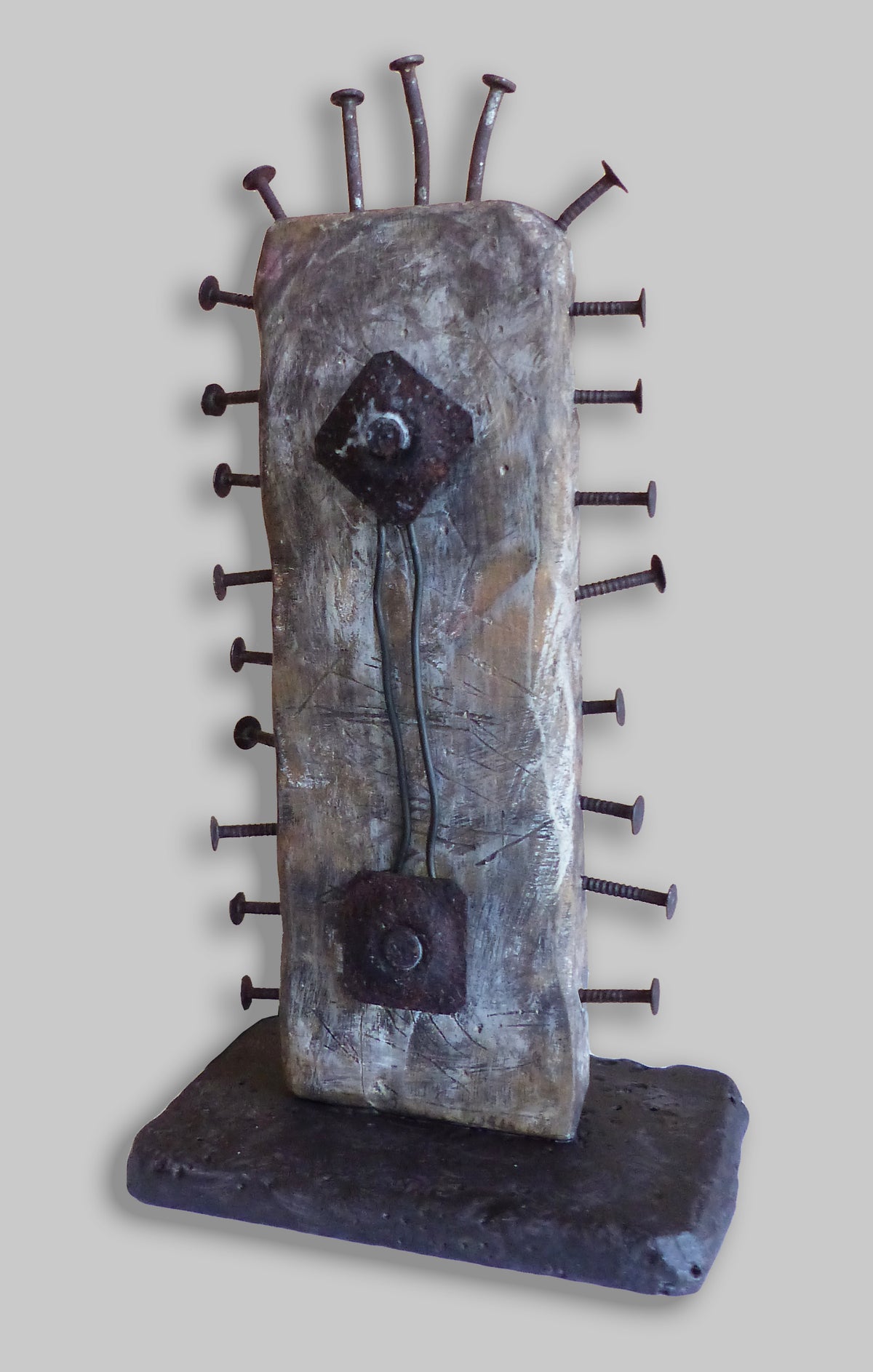 An abstract sculptural art piece featuring  with protruding metal nails, two dark metal circular elements, and a dark base.
